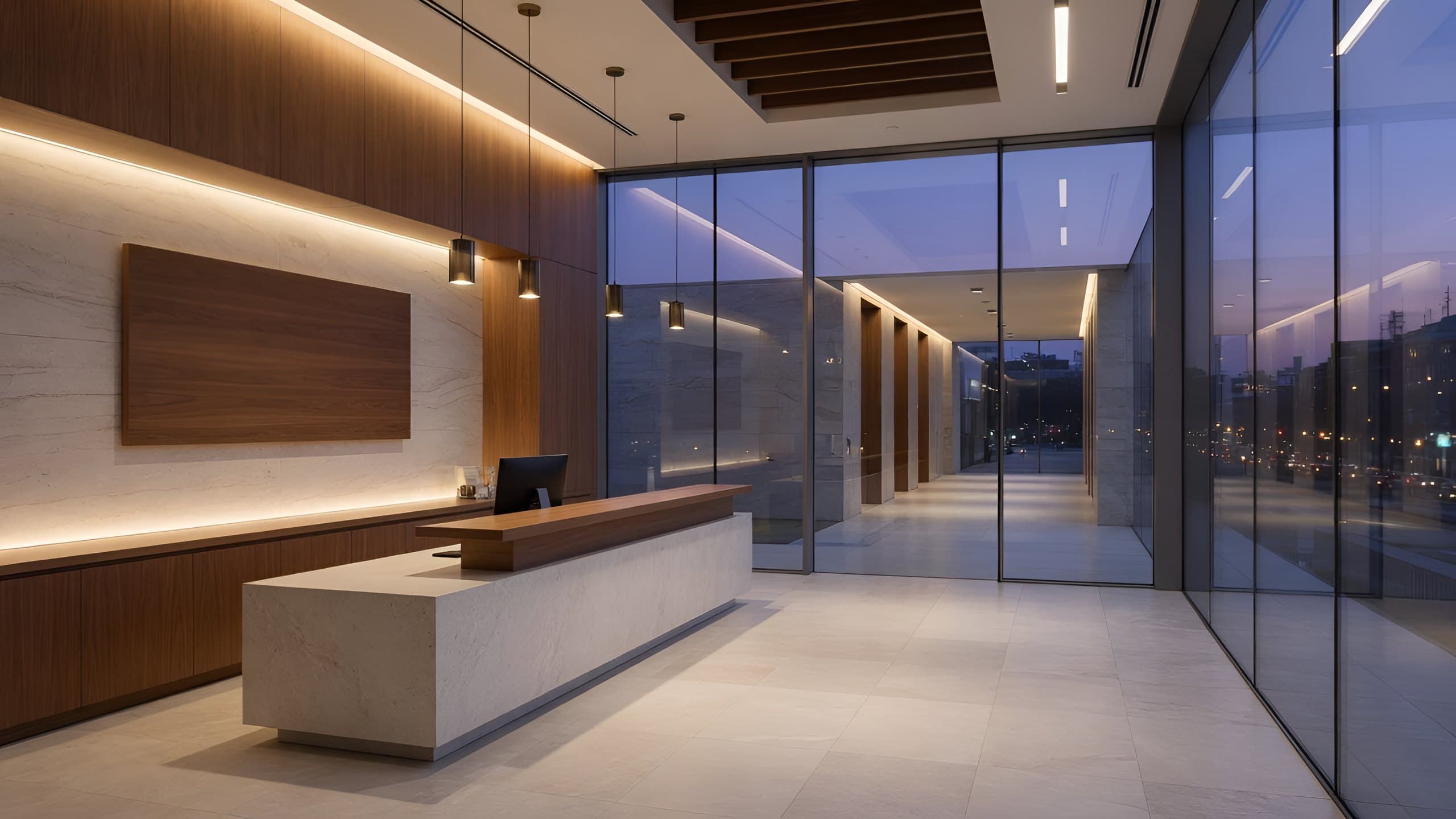 A hotel-style office lobby at dusk: reception desk on the left, a tall glass wall facing the entrance