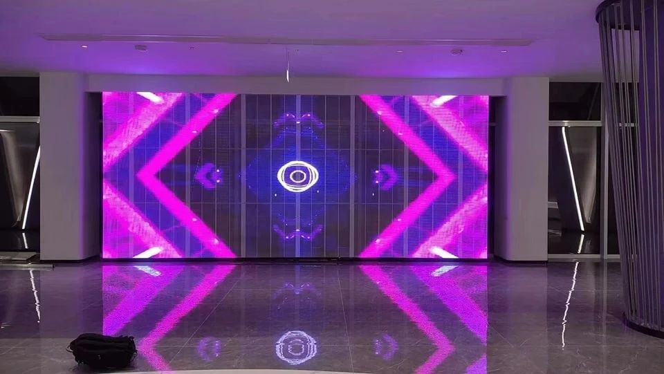 Large transparent LED wall in a lobby running bright magenta and blue geometric content, reflected in the polished floor